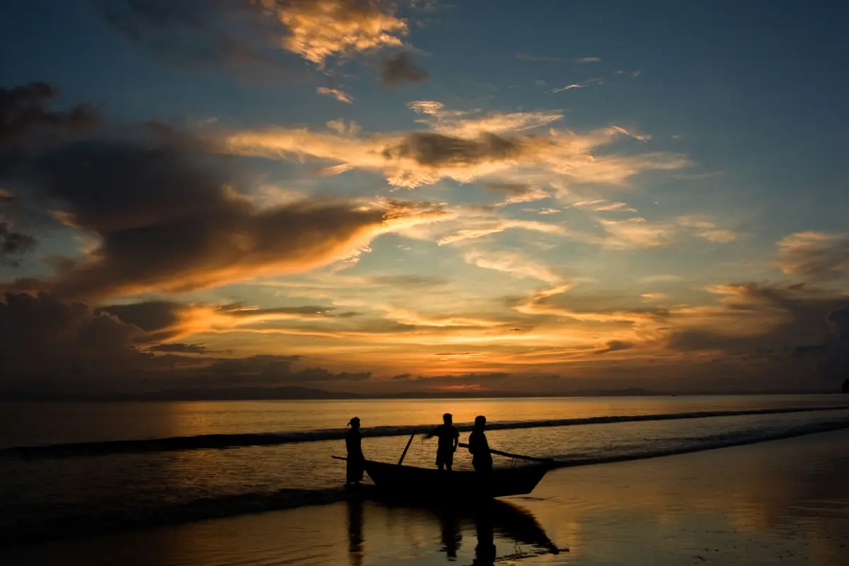 Fishing boat and silhouetted figures against an orange sunset over the Andaman Sea